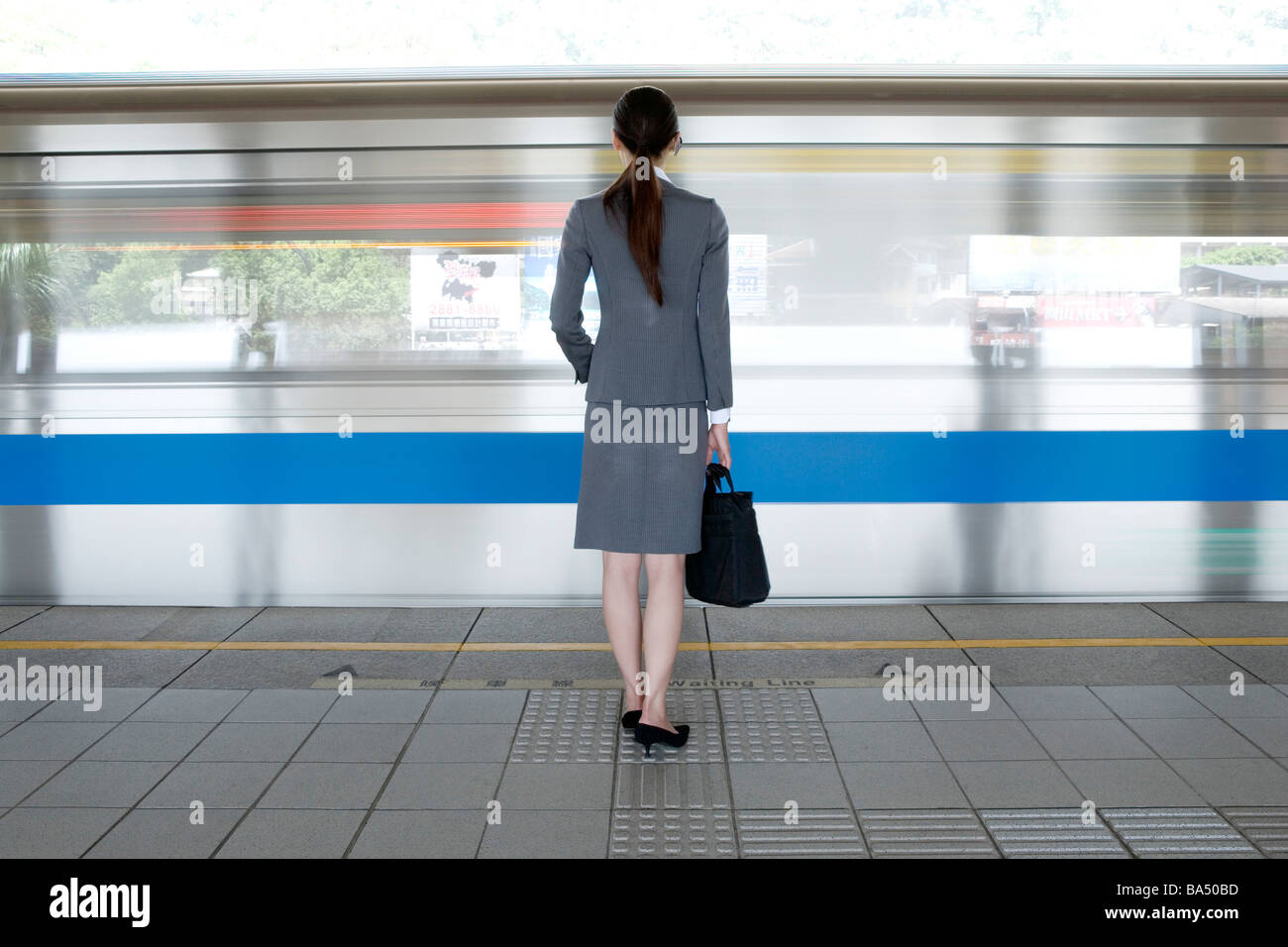 Imprenditrice con valigetta in piedi sulla piattaforma del treno vista posteriore Foto Stock