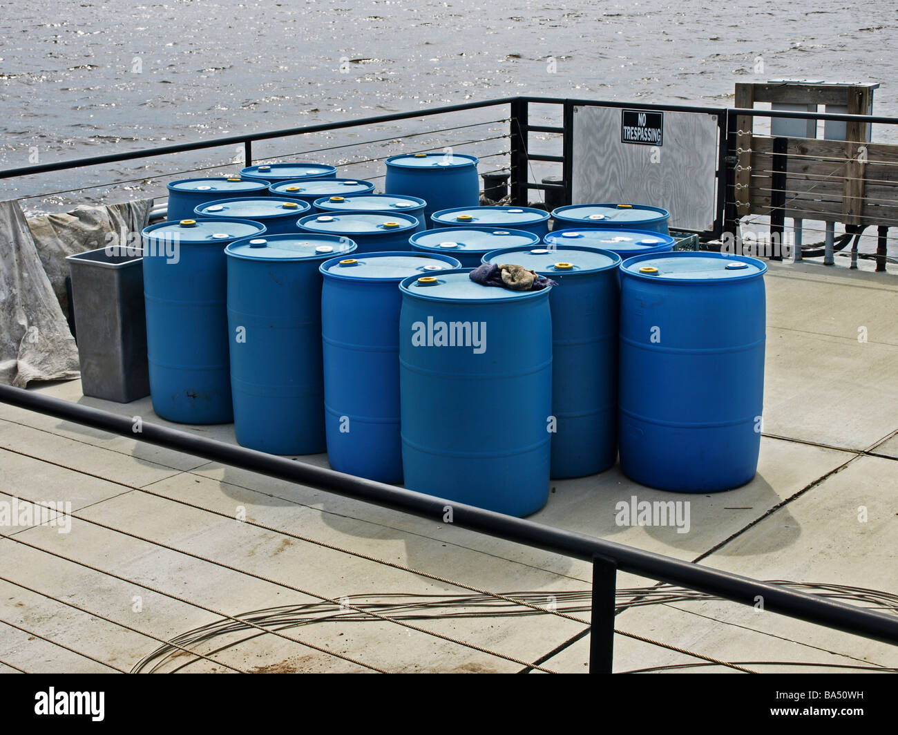 Blu petrolio barili di carburante su una banchina in legno dal fiume, acqua in background e la zona è circondata da una ringhiera rampa industrial Foto Stock