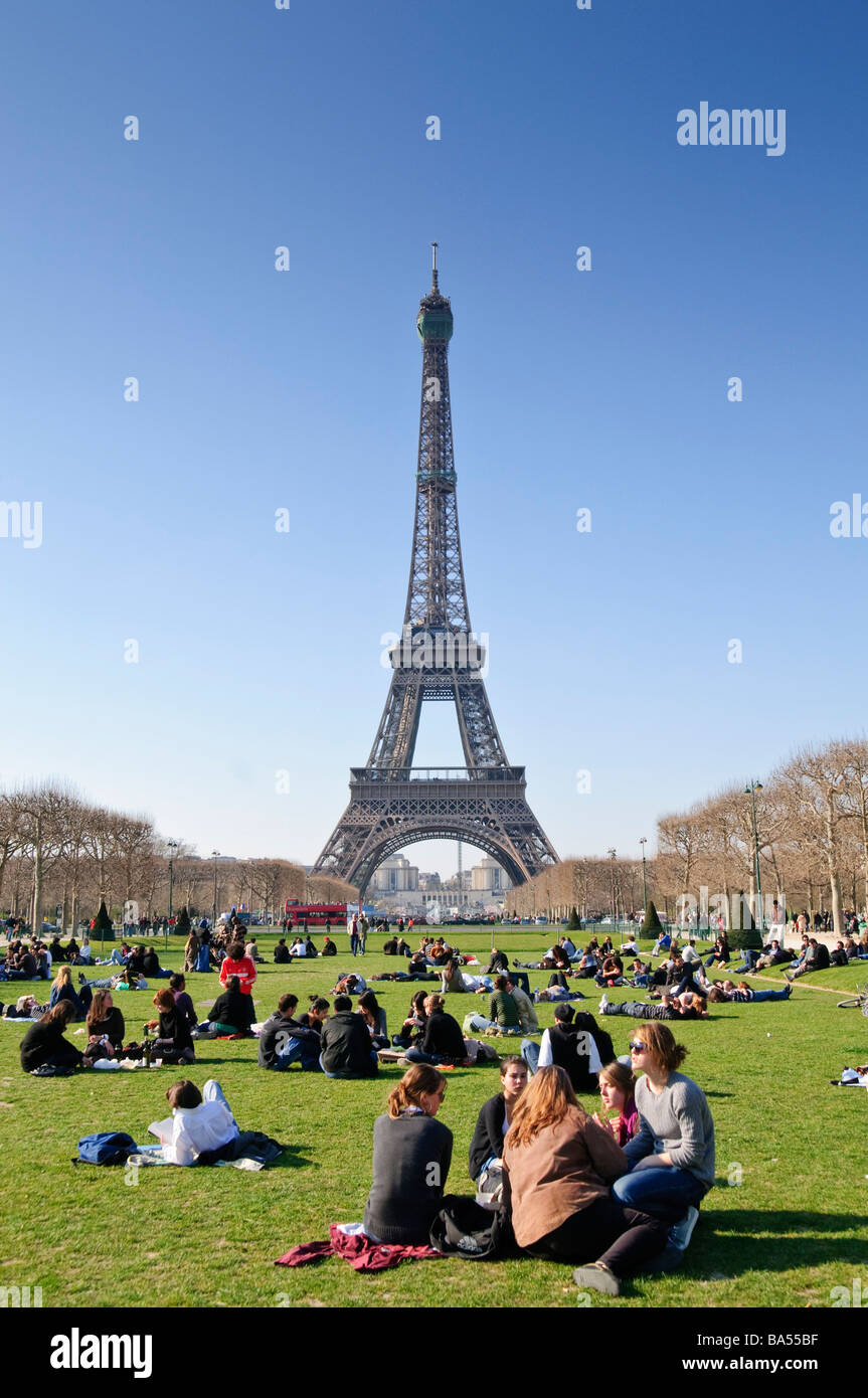 Torre Eiffel dal Parco Champ De Mars persone mattutine di primavera che rilassano Parigi Francia // PARIGI, Francia - persone che si rilassano sui prati verdi del Champ de Mars, un grande spazio verde pubblico, con la Torre Eiffel (Tour Eiffel) in primo piano sullo sfondo. La Torre Eiffel, una torre di ferro a reticolo sul campo di Marte, è stata costruita per l'esposizione mondiale del 1889 ed è alta 330 metri (1.083 piedi). Questo popolare parco, che prende il nome dal campo romano Marzio ("campo di Marte"), si estende dalla Torre Eiffel all'École Militaire. I visitatori e la gente del posto si godono il bel tempo in una mattina primaverile limpida Foto Stock