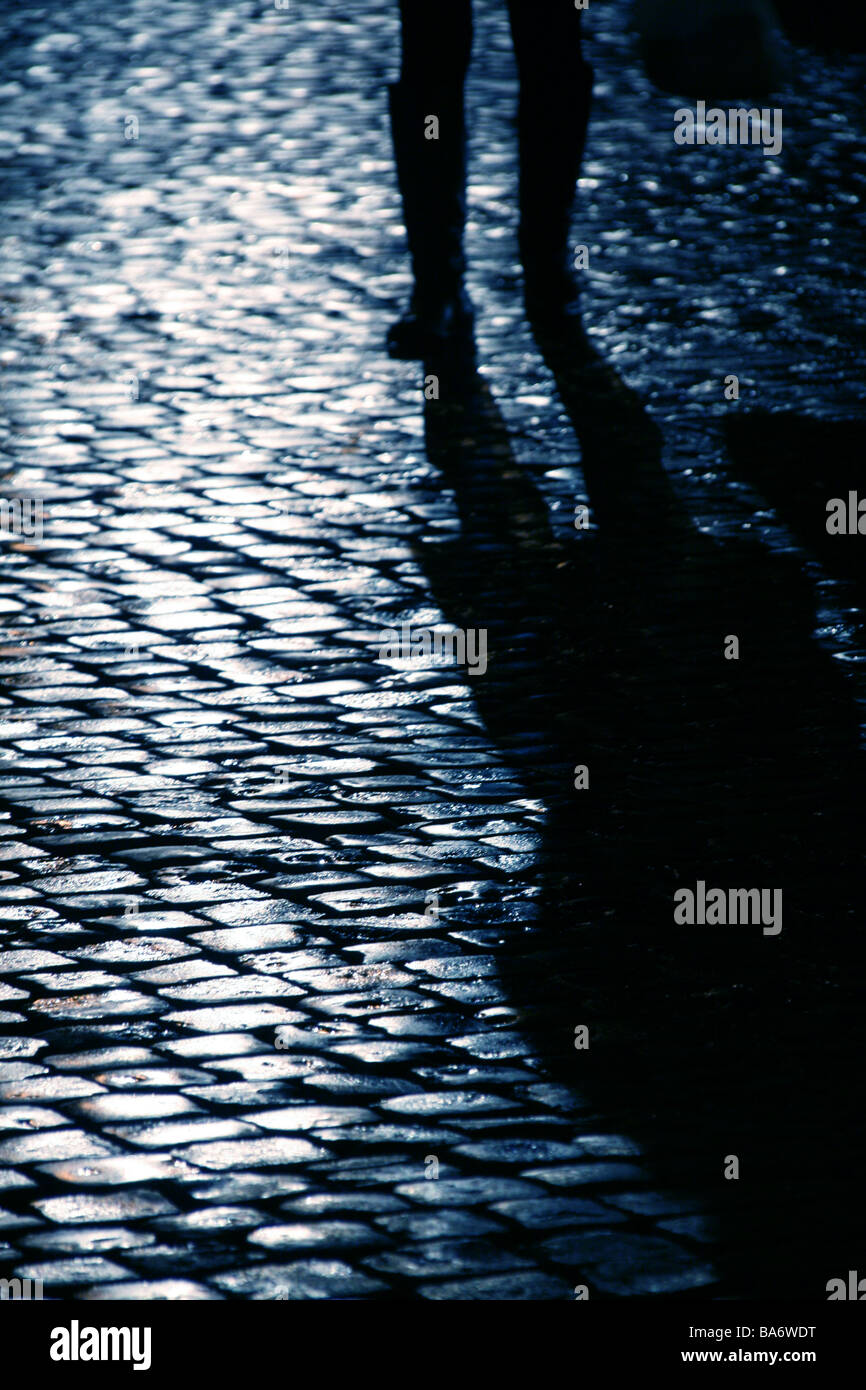 Persona che cammina sul bagnato strada di ciottoli di notte Foto Stock