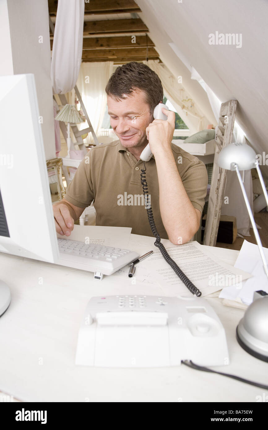 Studi uomo desk funziona Telefoni computer sorrisi semi-portrait appartamento uso ufficio persone 40-50 anni freelance indipendente Foto Stock