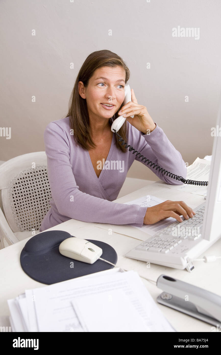 Studi donna desk funziona Telefoni computer sorrisi semi-portrait appartamento uso ufficio persone 40-50 anni freelance indipendente Foto Stock