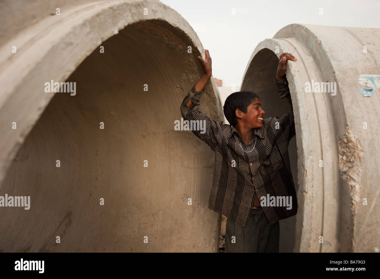 Un ragazzo indiano gioca tra tubi di fognatura di fronte ad una zona di costruzione in Gurgaon una città satellite a sud-ovest di Delhi Foto Stock