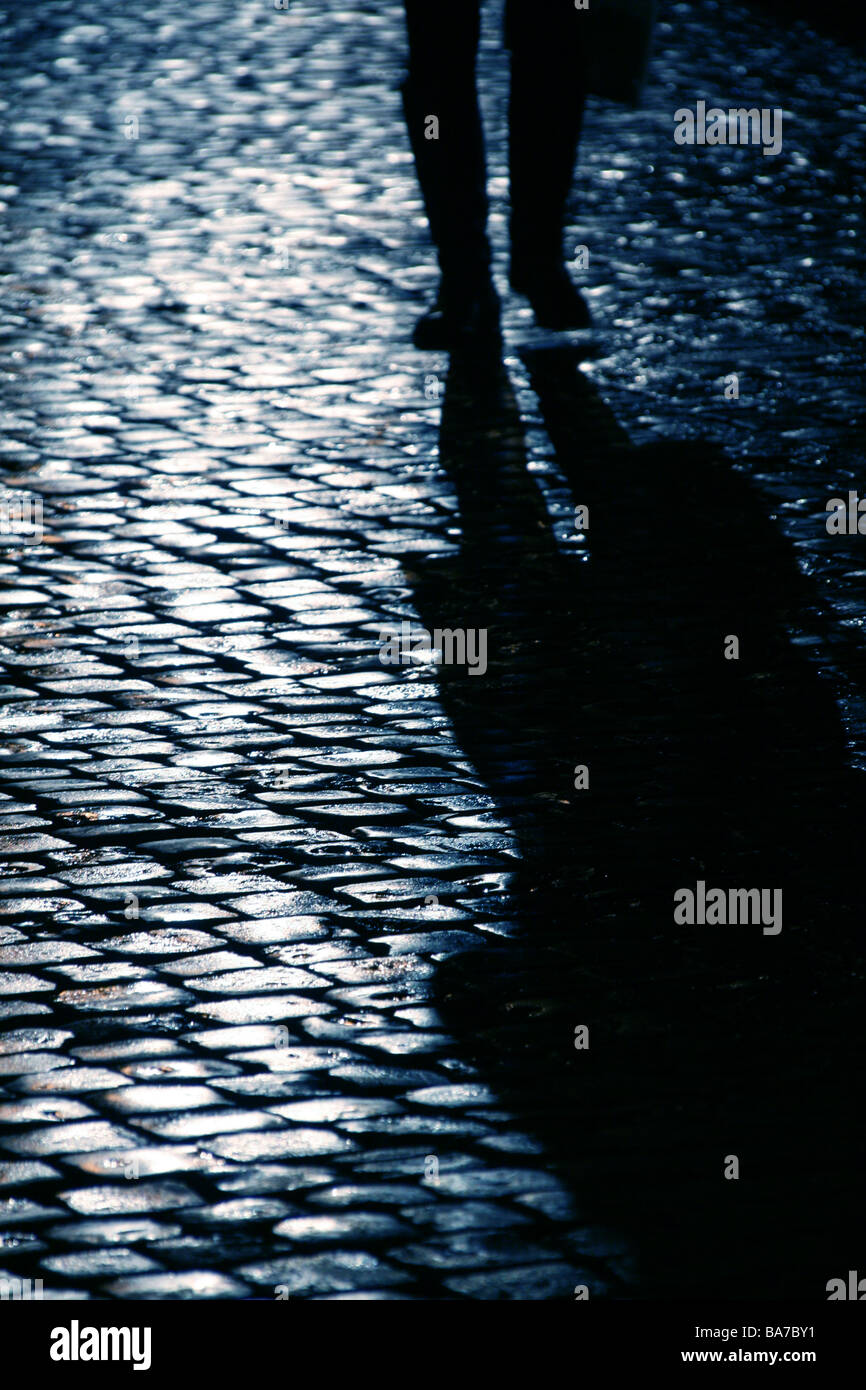 Persona che cammina sul bagnato strada di ciottoli di notte Foto Stock