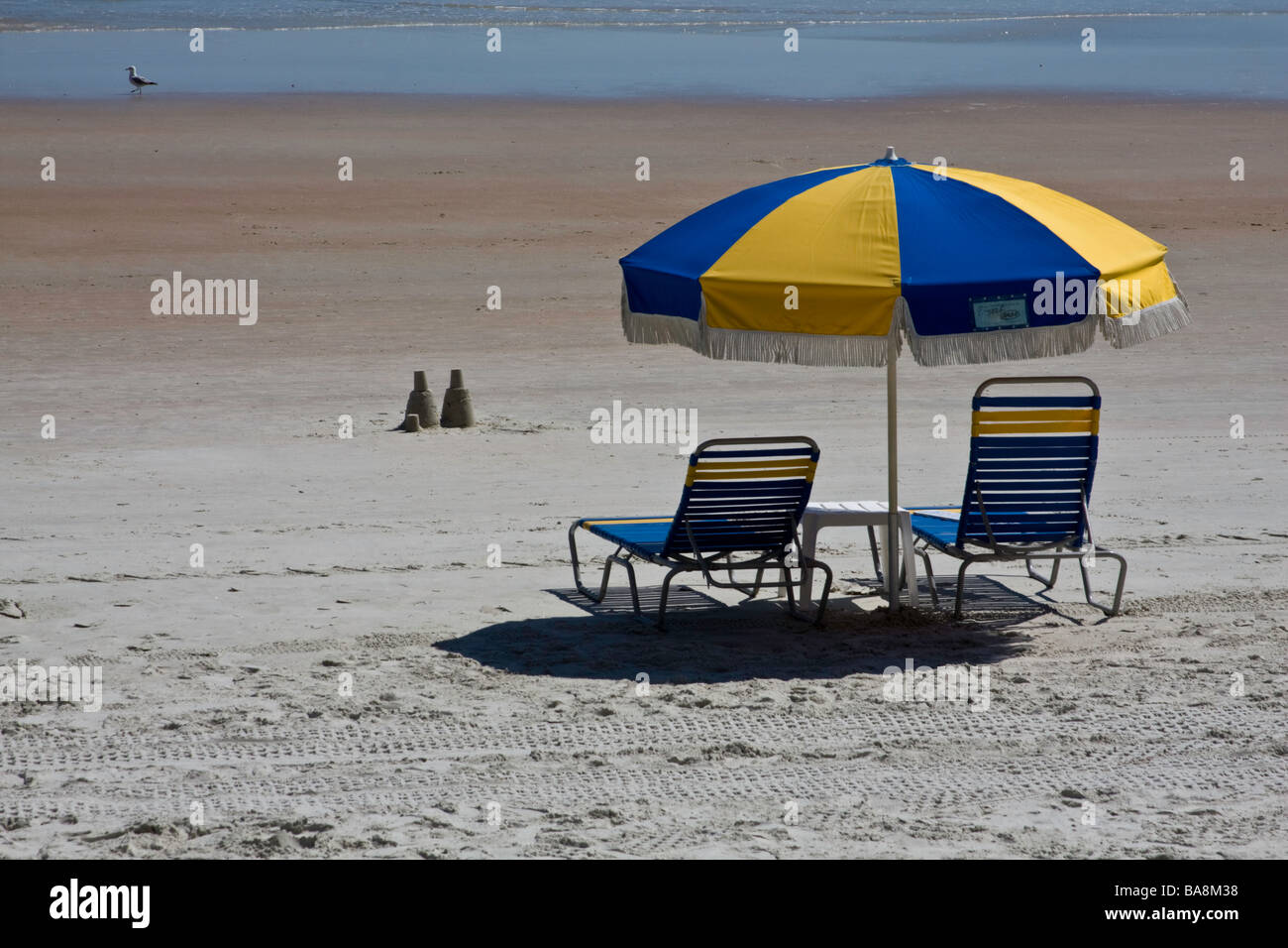 Due lone castelli di sabbia di sedersi di fronte due sedie vuote sulla spiaggia durante la pausa di primavera segnando una tendenza al ribasso nell'economia Foto Stock