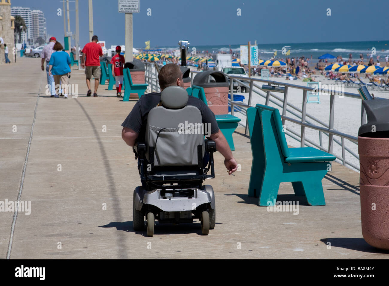 Persona con handicap a ruote lungo la spiaggia in una località turistica per visitare i siti turistici e giornata di sole. Foto Stock
