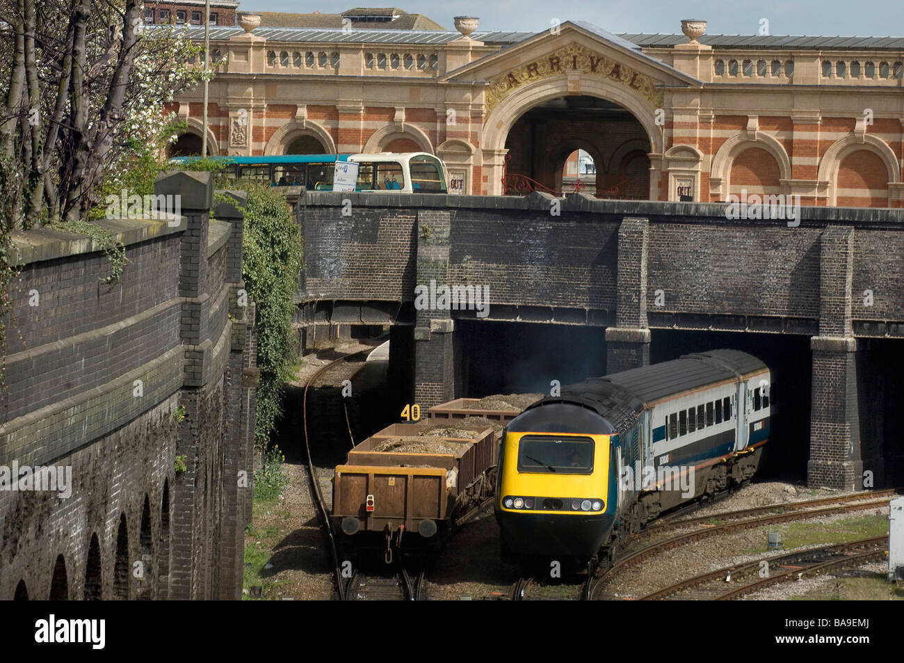 Un treno merci andare sotto un ponte come un treno passeggeri ed emerge un bus è visibile sulla strada sopra Foto Stock