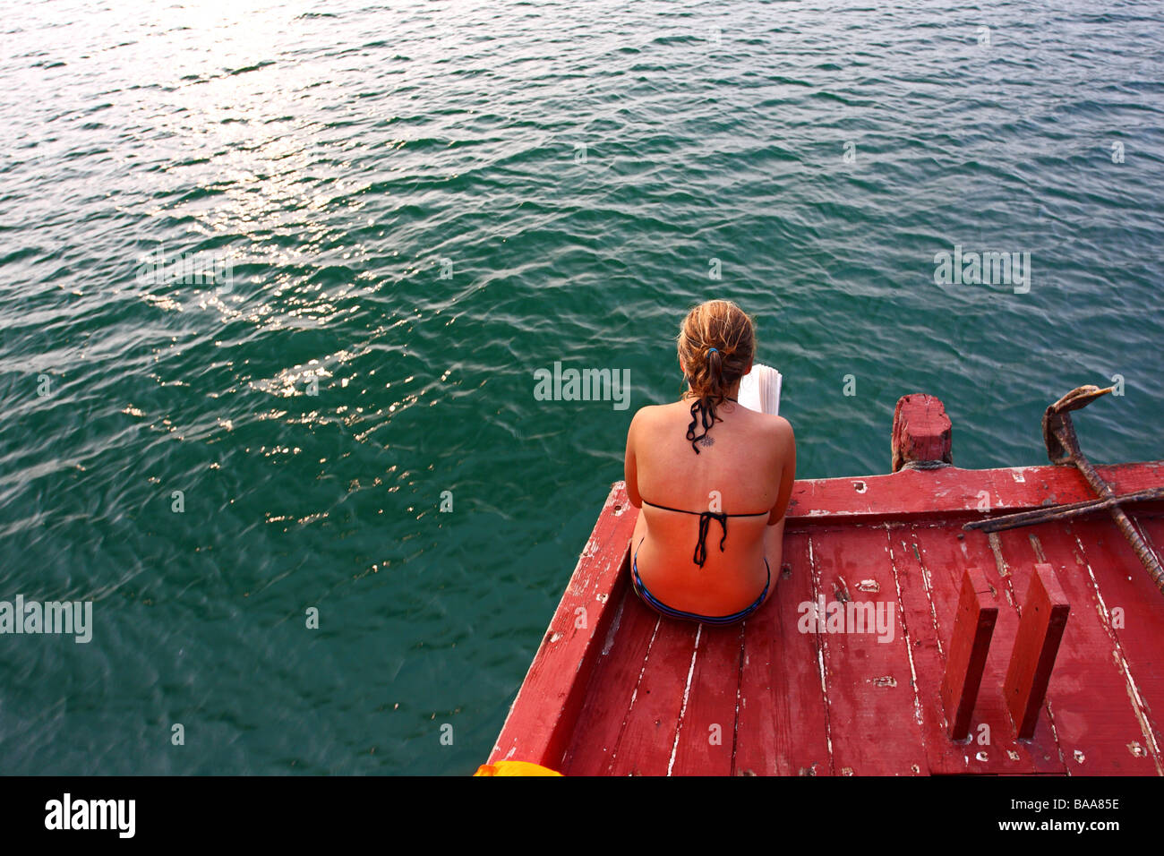 Ragazza a leggere un libro sul ponte di una nave da crociera della baia di Halong, Vietnam Foto Stock