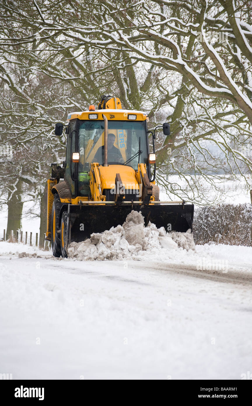 JCB essendo utilizzato per cancellare una coperta di neve strada di campagna in Inghilterra al tempo di inverno Foto Stock