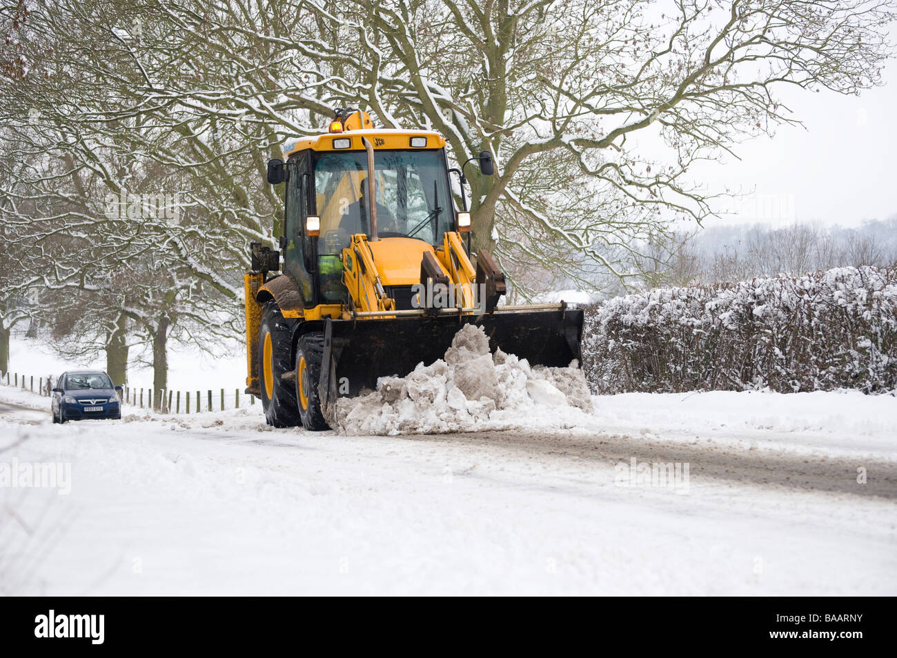 Auto in seguito ad una cancellazione JCB una coperta di neve strada di campagna in Inghilterra al tempo di inverno Foto Stock