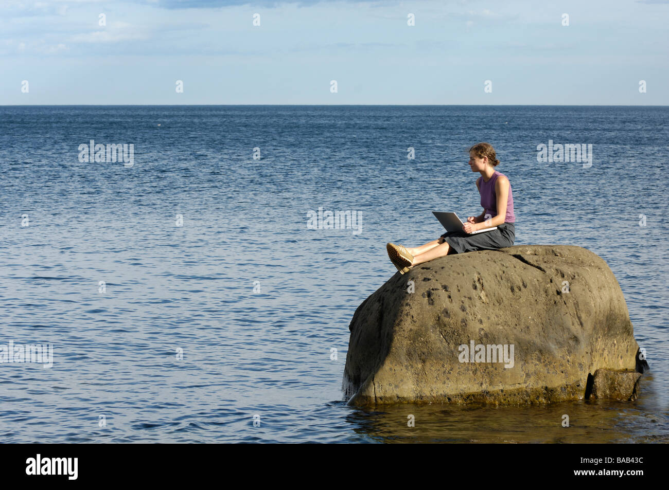 Una donna che utilizza un computer portatile seduto su una scogliera, Vaddo,, arcipelago di Stoccolma, Svezia. Foto Stock