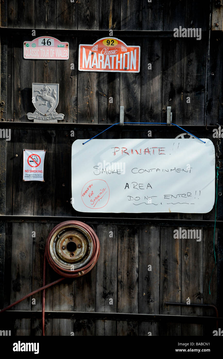 Un rustico in legno porta di garage con vecchi segni automotive e un handmade segno privati visitatori di avvertimento di fumo di sigaretta. Foto Stock