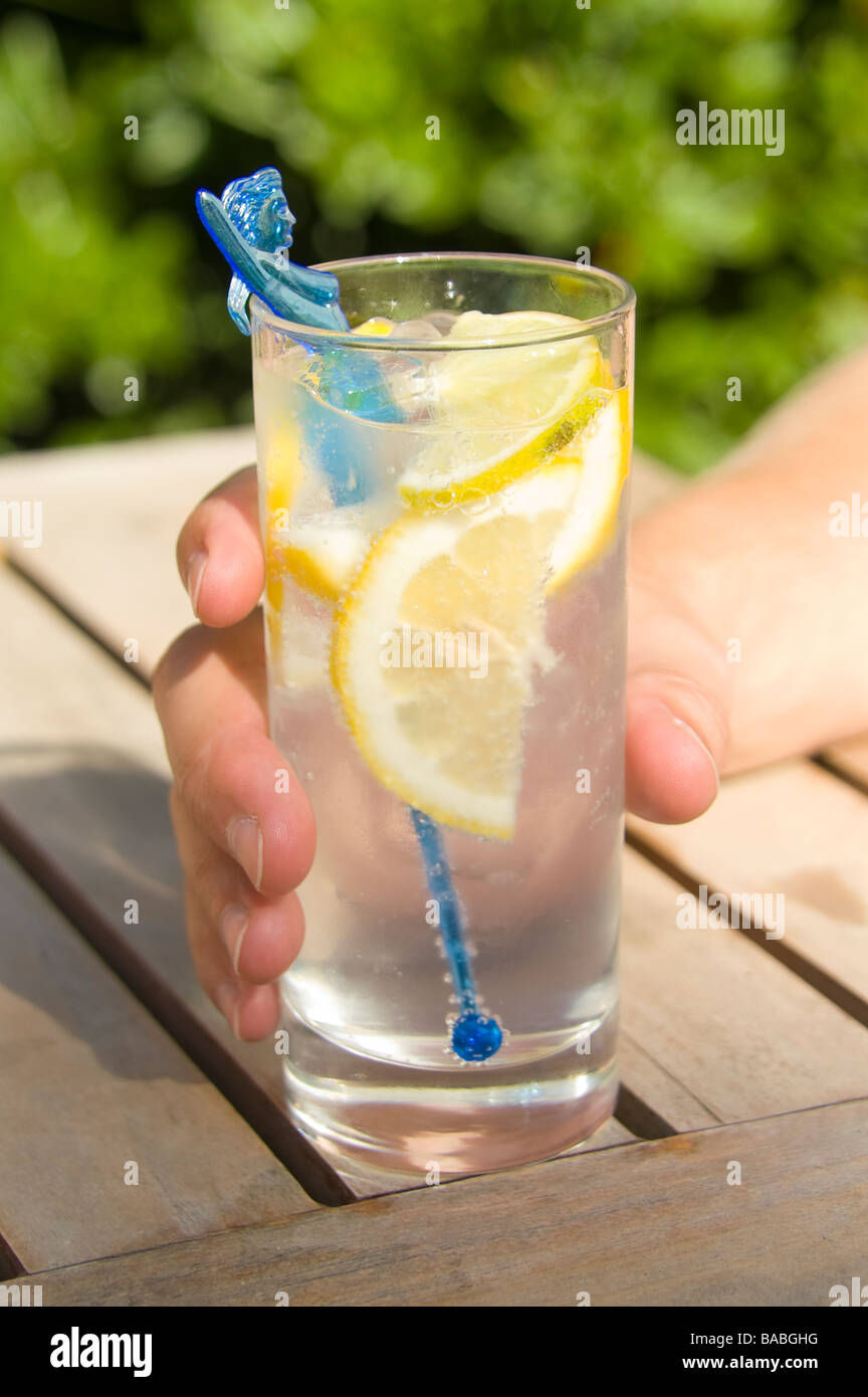 Mano che regge un bicchiere di Gin Tonic con una fettina di limone e un blu  miscelatore mermaid Foto stock - Alamy