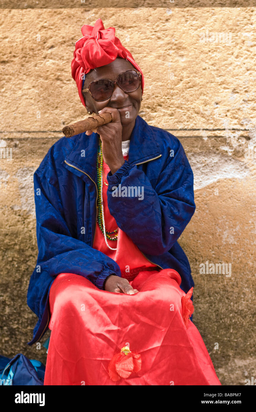 Donna anziana in un copricapo rosso fuma un sigaro di grandi dimensioni in Havana Vieja. Foto Stock