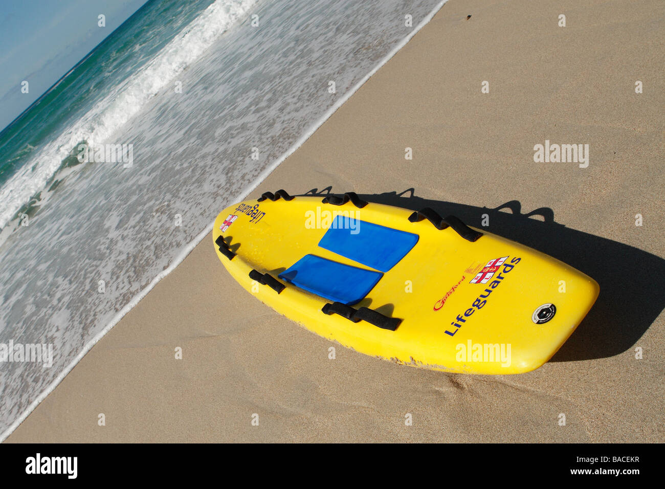 Bagnino RNLI giallo di salvataggio della tavola da surf sulla spiaggia sabbiosa a Sennen Cornwall con l'Oceano Atlantico mare Foto Stock