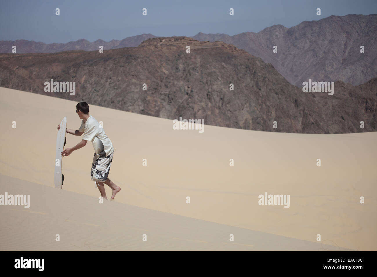 Il boarder sabbia Camminare indietro fino la duna con il pittoresco sfondo del deserto del Sinai Foto Stock
