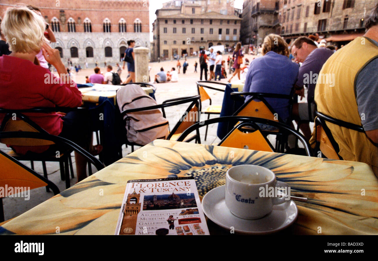 Un vuoto che la tazza di caffè si siede su un tavolo accanto a un libro guida a Firenze Italia con altri commensali seduti in piazza Foto Stock