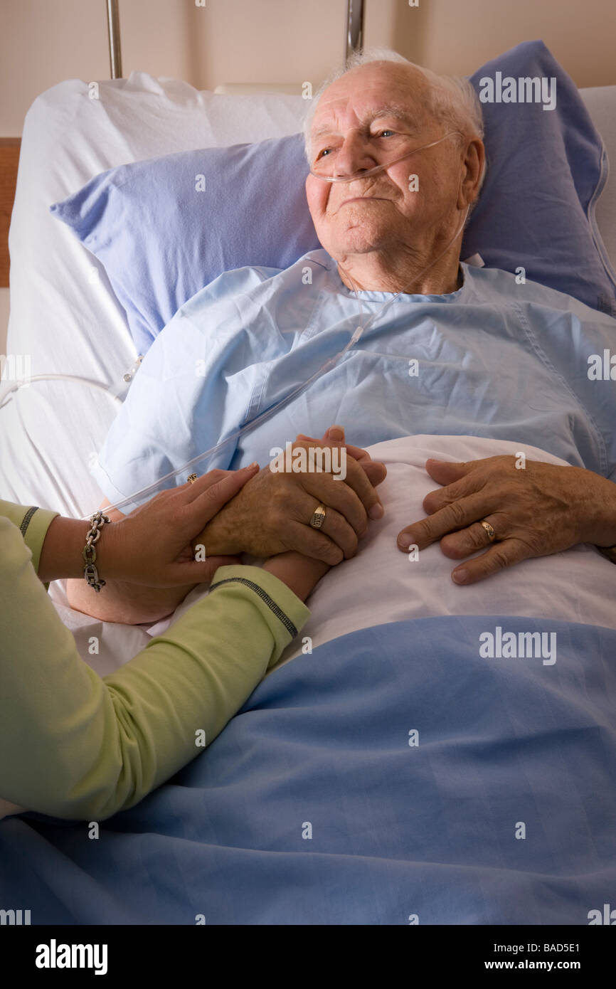 Uomo in un letto di ospedale; mano d'uomo essendo trattenuto da una donna Foto Stock