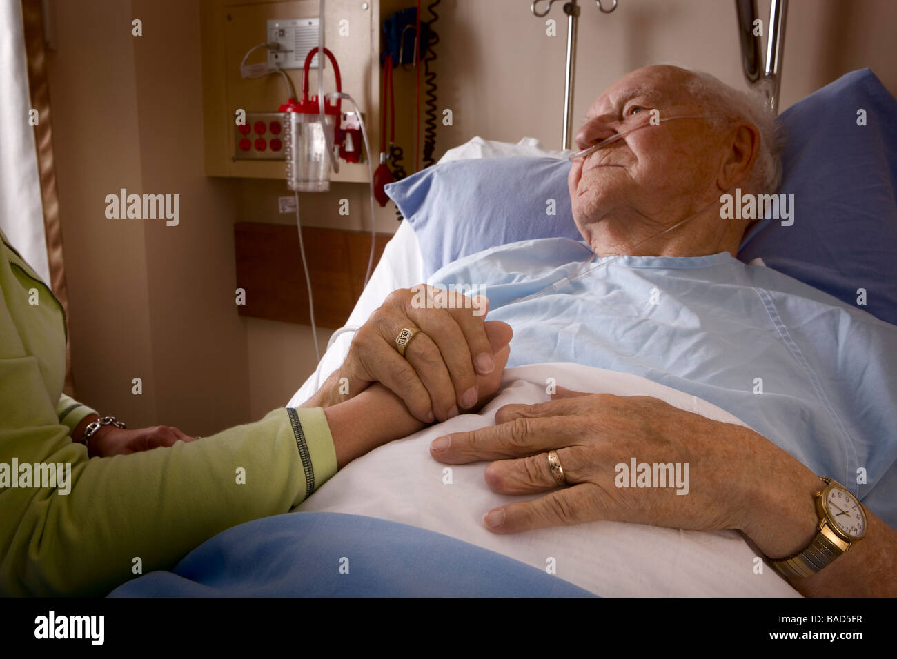 Uomo in un letto di ospedale; mano d'uomo essendo trattenuto da una donna Foto Stock