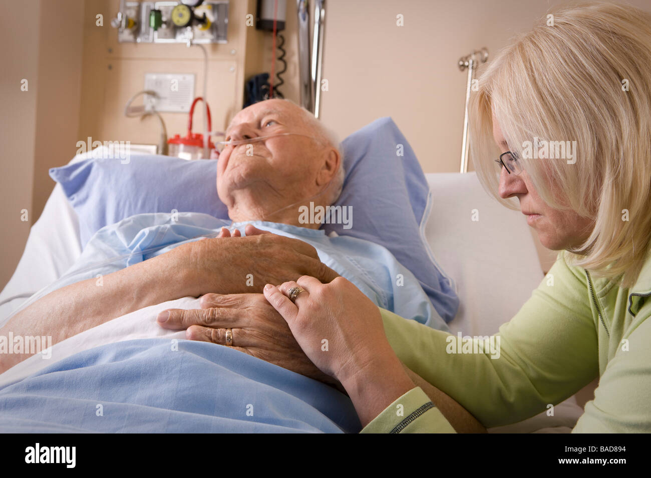 Uomo anziano e sua figlia; donna seduta da un uomo di letto di ospedale Foto Stock