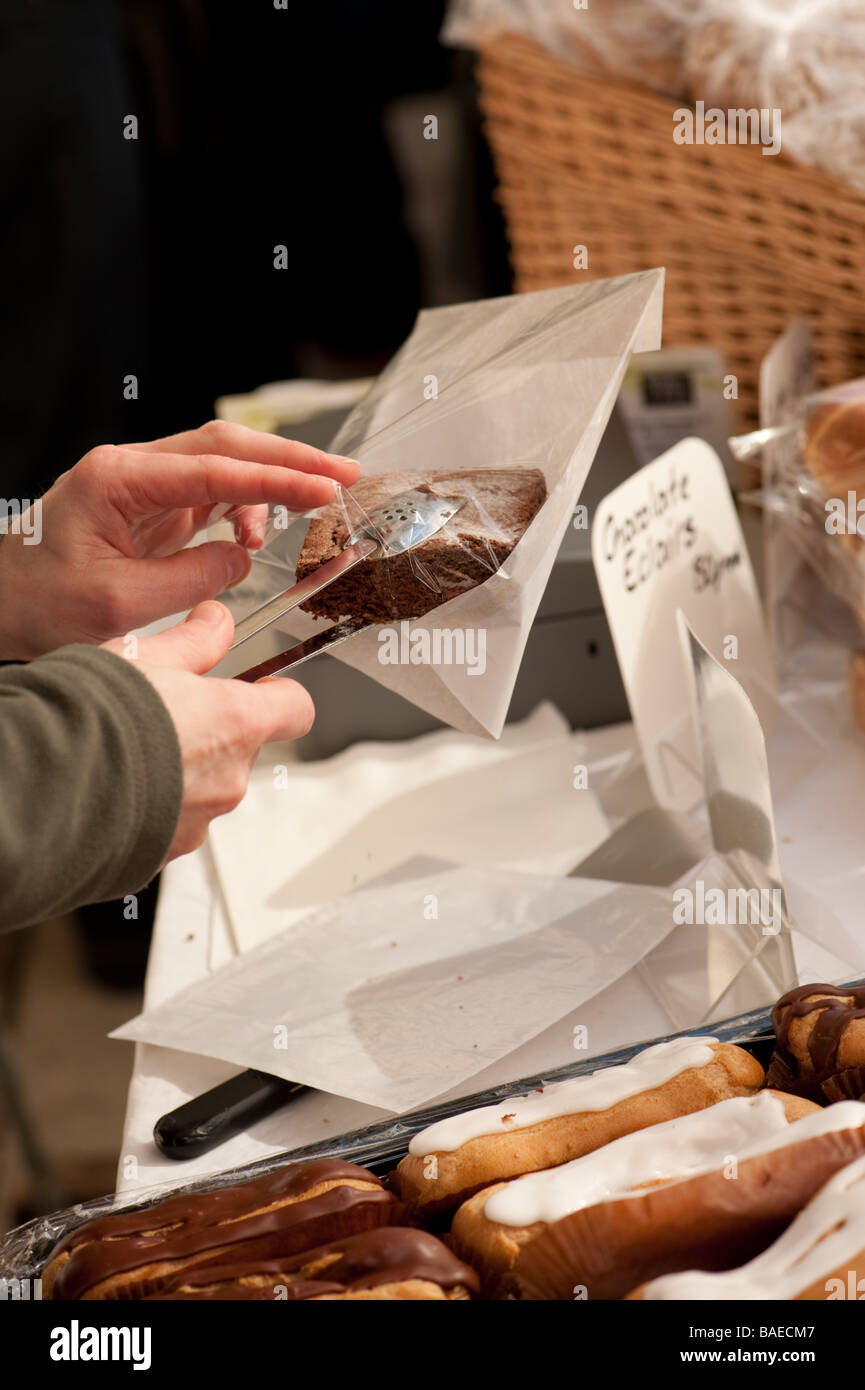 Persona che vende una porzione di casa sfornati freschi torta al cioccolato a Aberystwyth Farmers Market Wales UK Foto Stock