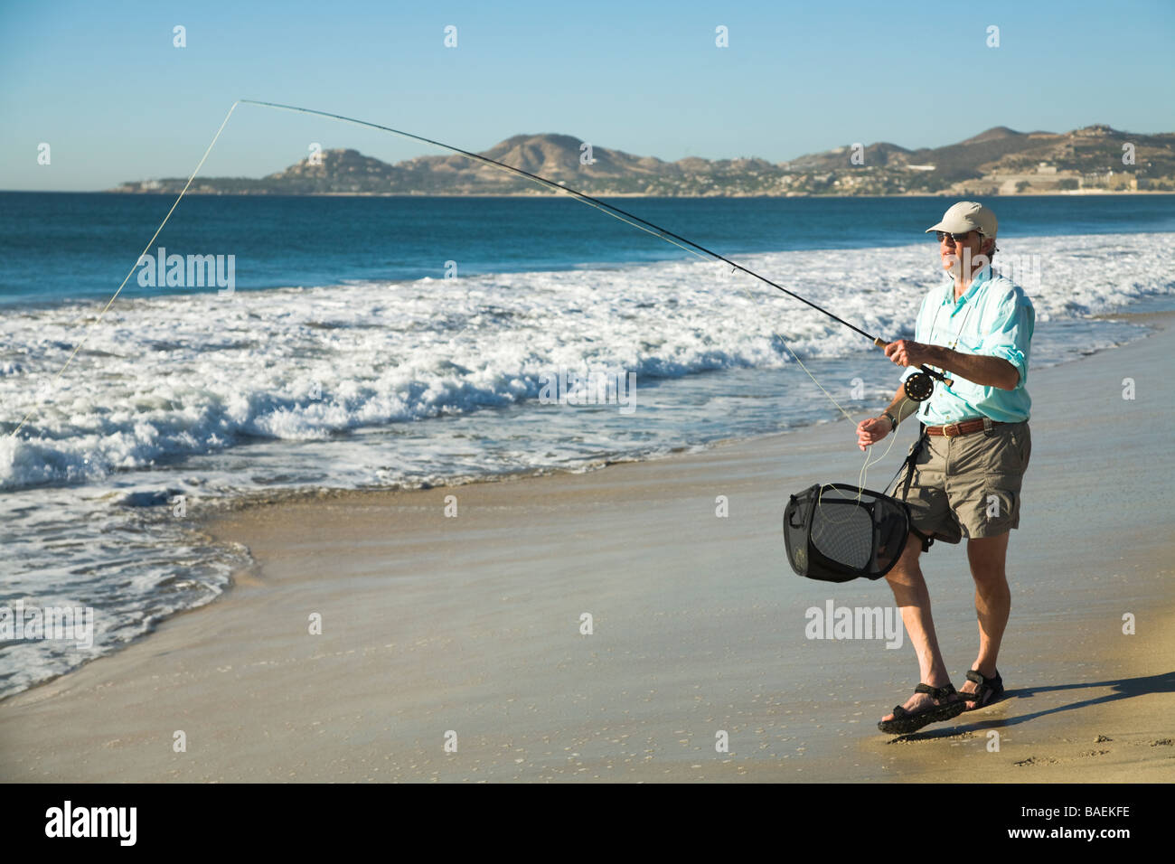 Messico San Jose del Cabo Caucasian uomo di mezza età di acqua salata di pesca a mosca nel mare di Cortez dalla spiaggia asta di trattenimento e bobina Foto Stock