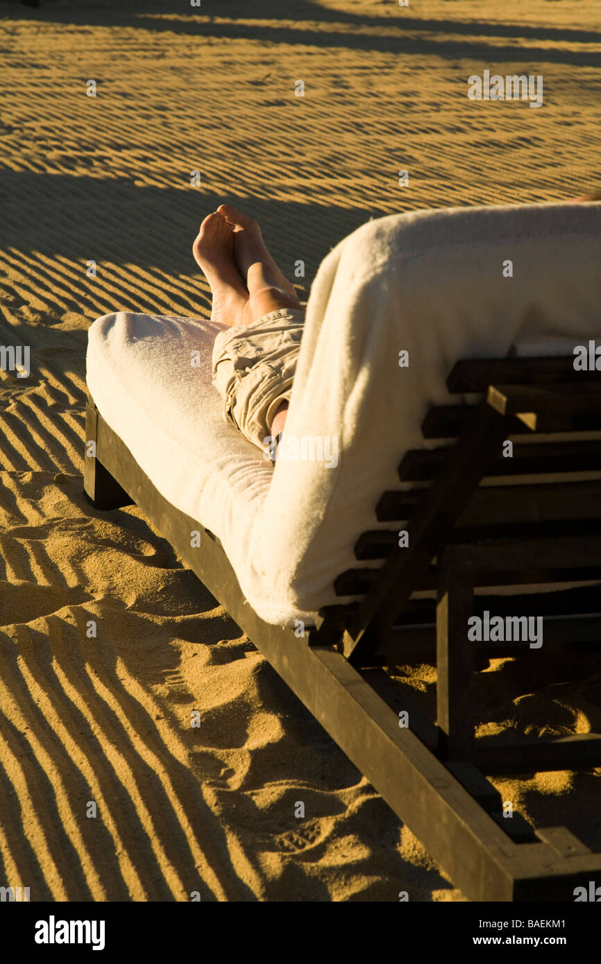 Messico San Jose del Cabo dei piedi e delle gambe di uomo che indossa pantaloncini seduto sulla chaise longue su rastrellata spiaggia sabbiosa Foto Stock