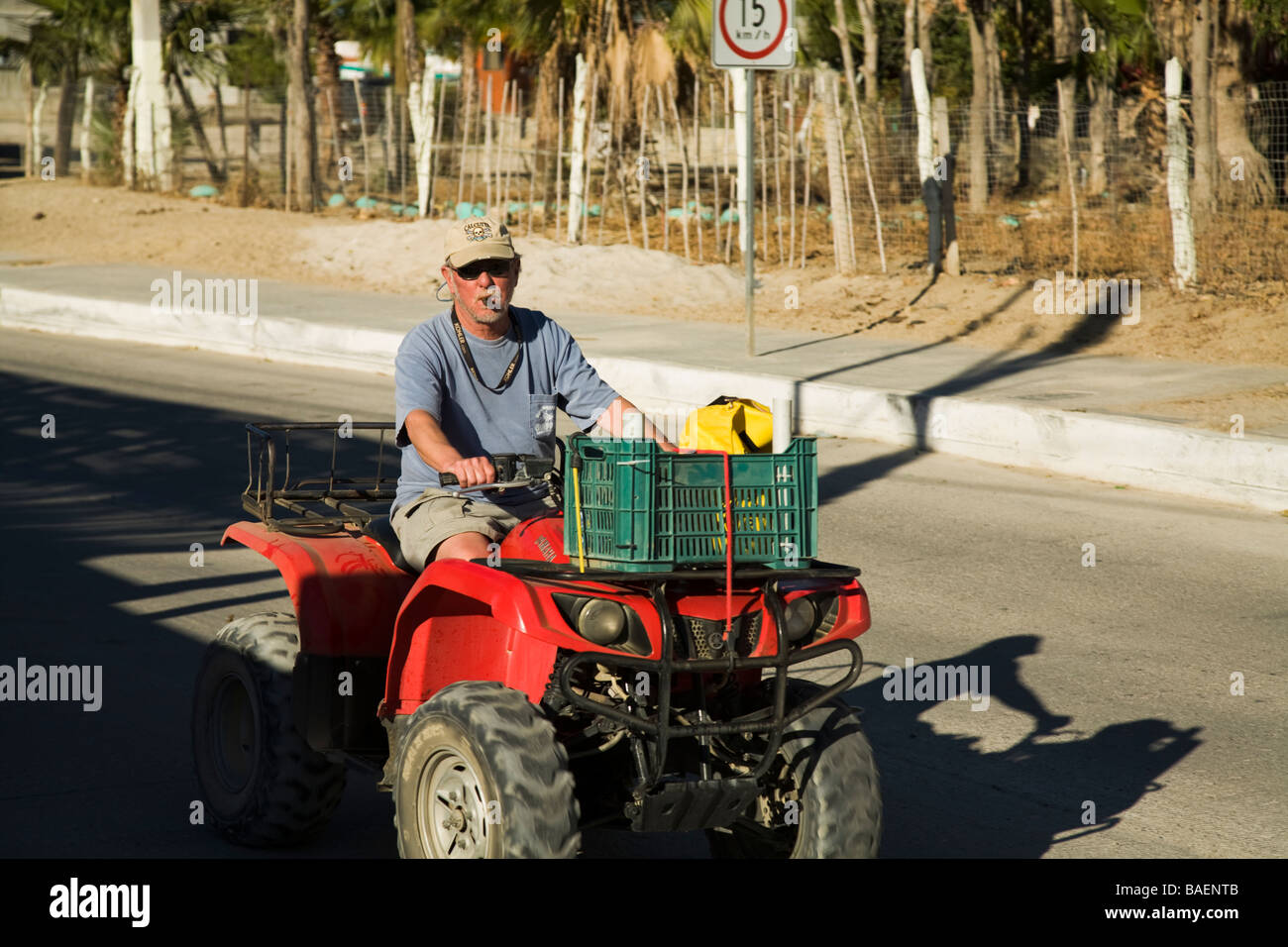 Messico Los Barriles pensionati American uomo alla guida di un ATV su strada in città e di fumare il sigaro Foto Stock