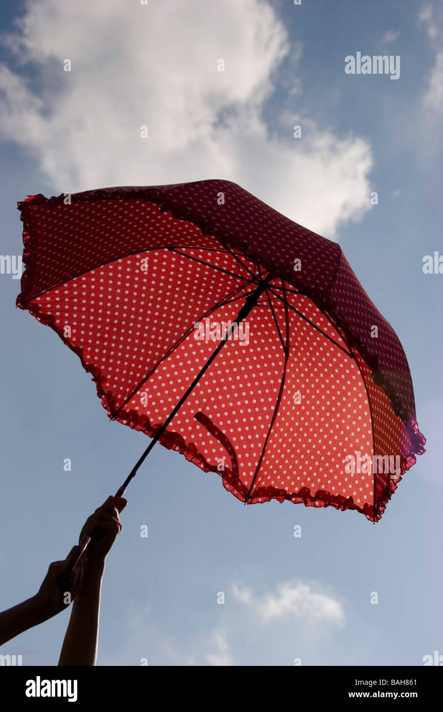 Il bianco e il rosso polka dot ombrello essendo trattenuto contro un cielo blu Foto Stock