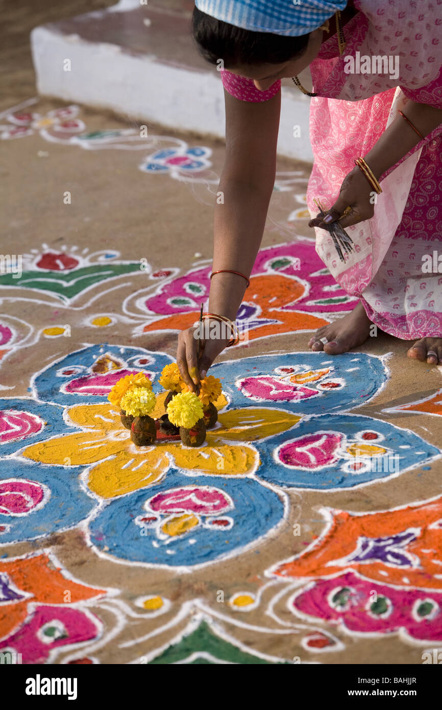 Donna indiana mettendo i bastoncini di incenso in un'offerta di fiori e di sterco di vacca su un Rangoli design in un Indiano street Foto Stock