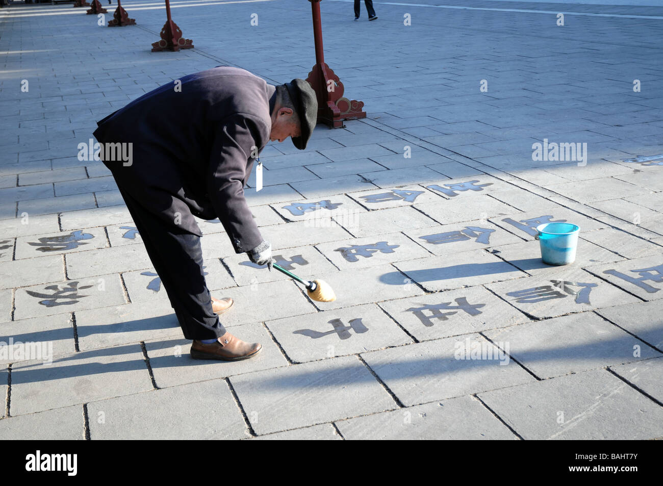 Il vecchio uomo cinese praticare la calligrafia acqua con una spazzola. Una visione comune in parchi e spazi pubblici in Cina. Foto Stock