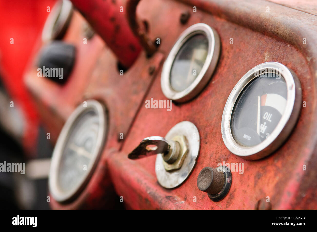 Rusty quadro della strumentazione di un rosso vintage trattore agricolo che mostra i quadranti, la chiave di accensione e del pulsante di avviamento Foto Stock