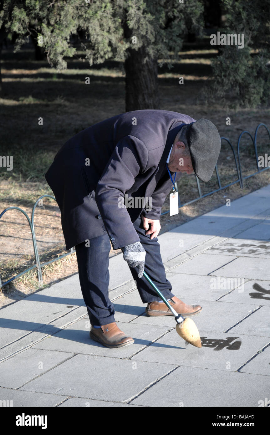 Il vecchio uomo cinese praticare la calligrafia acqua con una spazzola. Una visione comune in parchi e spazi pubblici in Cina. Foto Stock