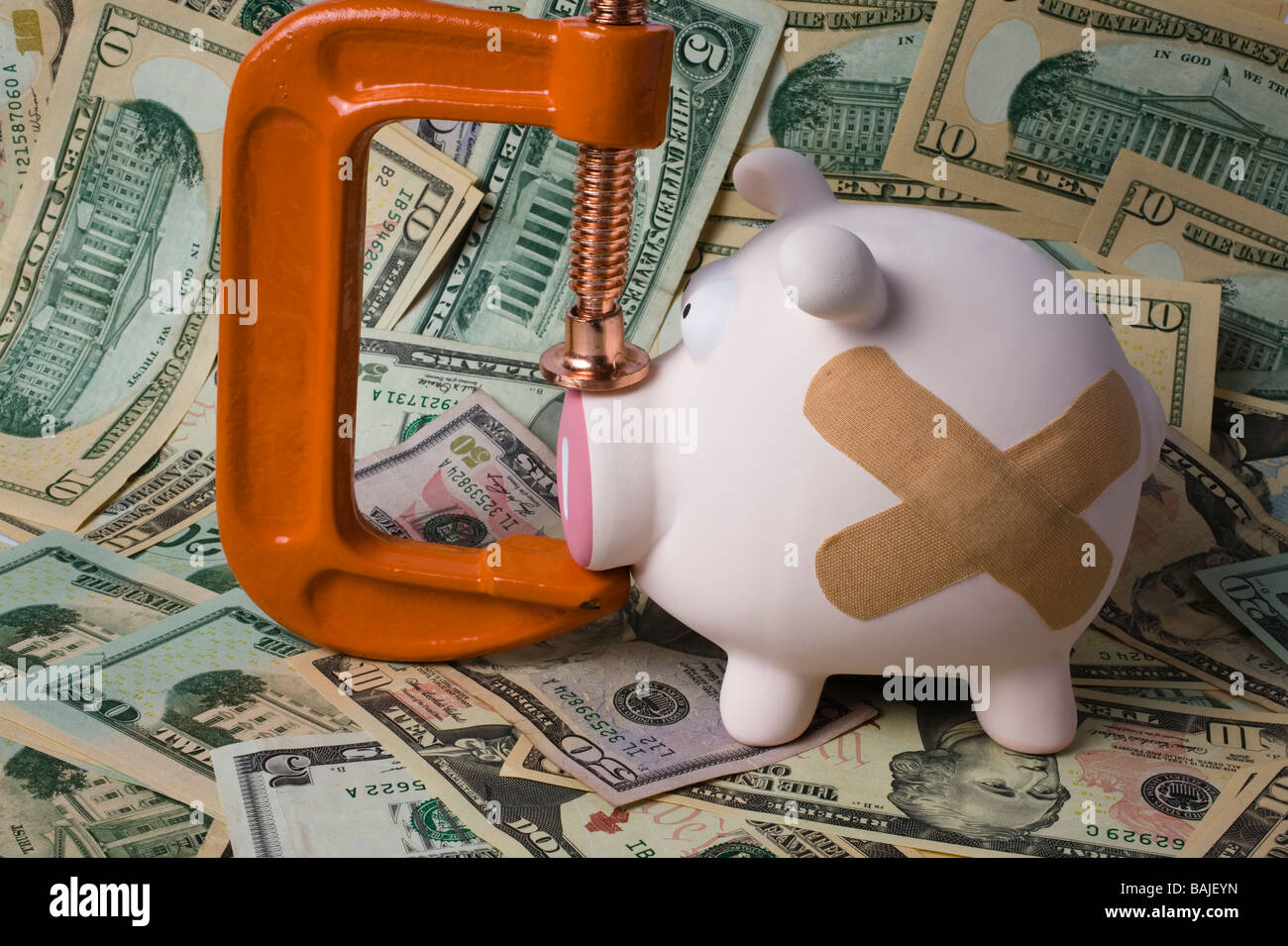 Salvadanaio con bende e un morsetto sul suo muso seduto su uno strato di dollari USA Foto Stock