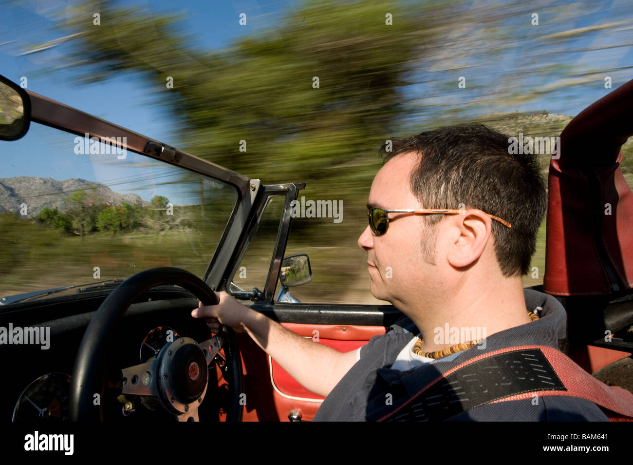 Uomo alla guida di un classico MG Midget sport cabriolet con il tetto verso il basso su una soleggiata giornata d'estate Foto Stock