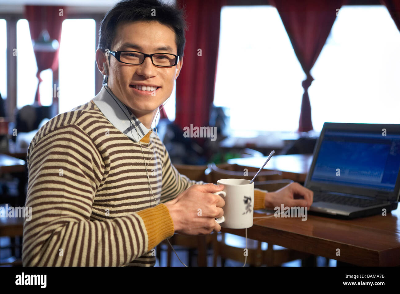 Giovane uomo seduto in Cafe con Computer Portatile Foto Stock