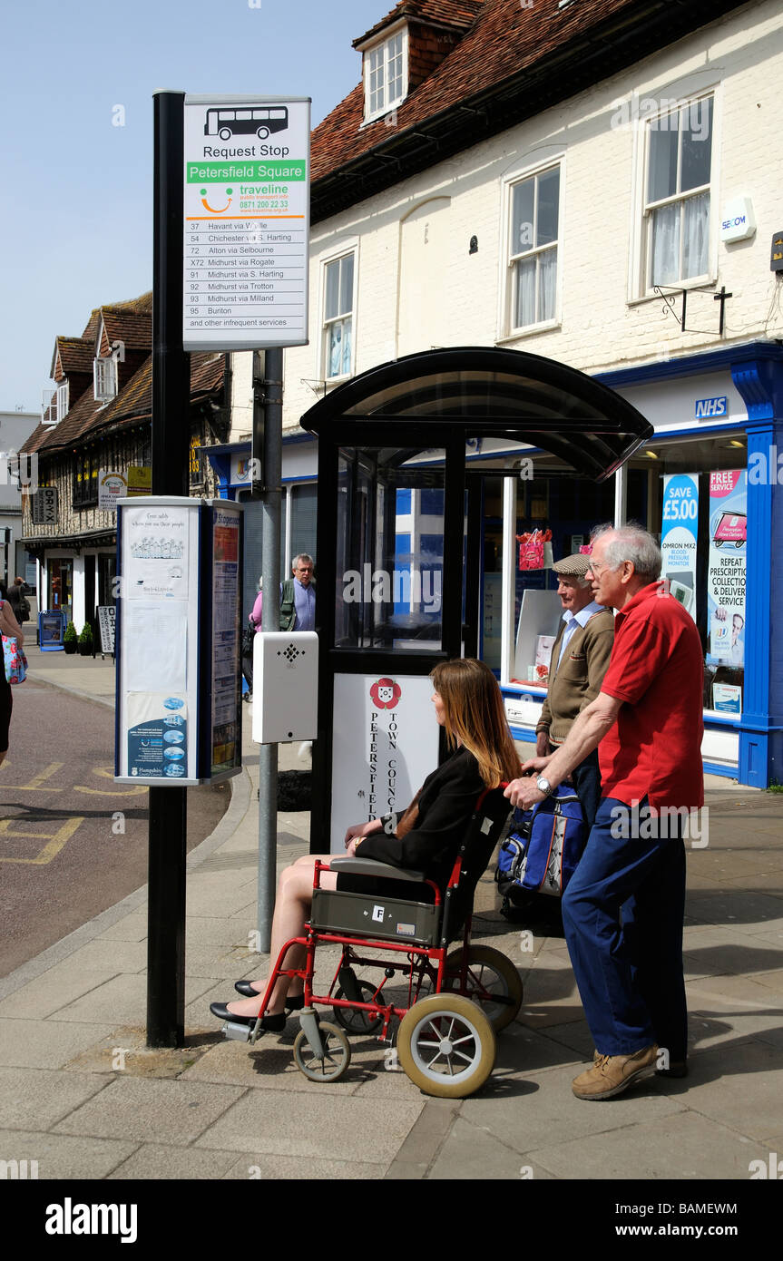 Femmina sedia a rotelle non valido utente e caregiver maschio controllare gli orari degli autobus ad una fermata del bus Foto Stock