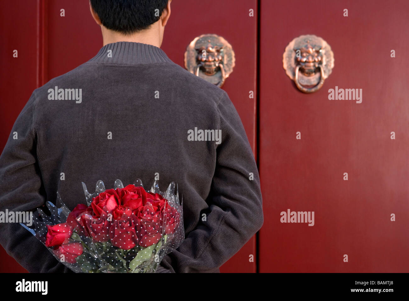 Giovane uomo in attesa davanti alla porta di casa con un mazzo di rose dietro la schiena Foto Stock