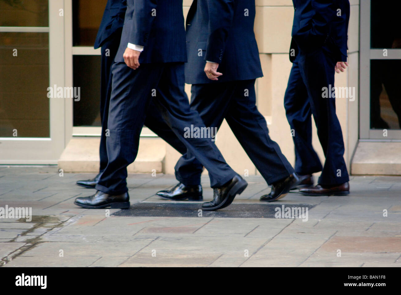 Gli uomini d' affari/Bankers in abbigliamento business a piedi a un ritmo sostenuto su una strada di città, come una squadra mentre uno è fuori fase Foto Stock