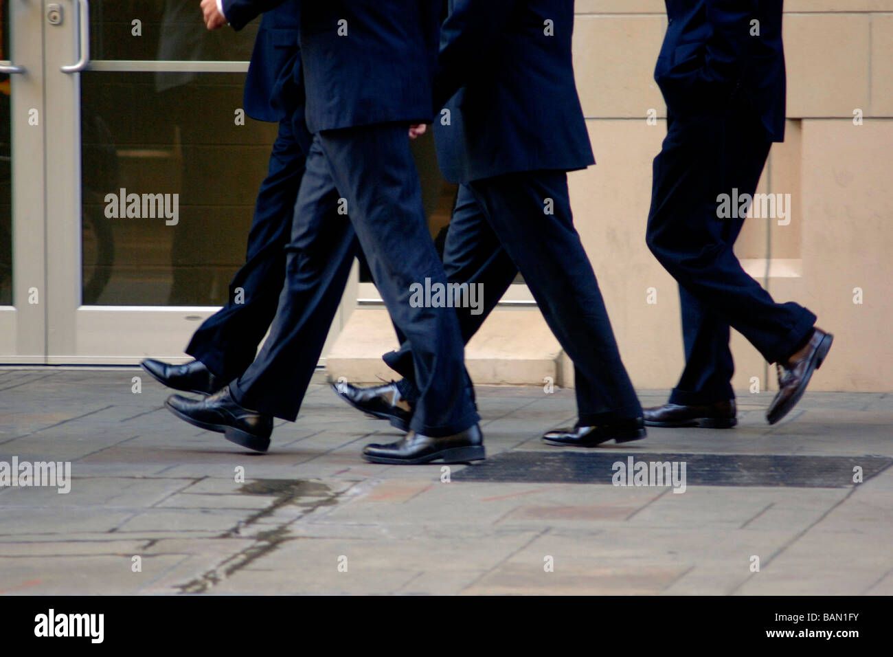 Gli uomini d' affari/Bankers in abbigliamento business a piedi a un ritmo sostenuto su una strada di città, come una squadra mentre uno è fuori fase Foto Stock