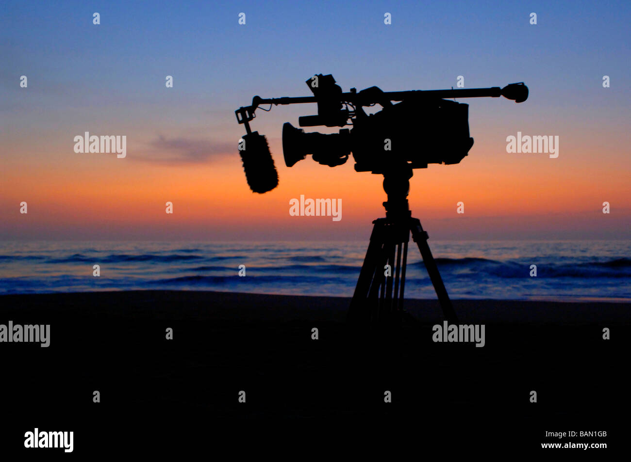 Silhouette di moto fotocamera su un treppiede con microfono boom e bella spiaggia tropicale onde per uno sfondo al tramonto Foto Stock