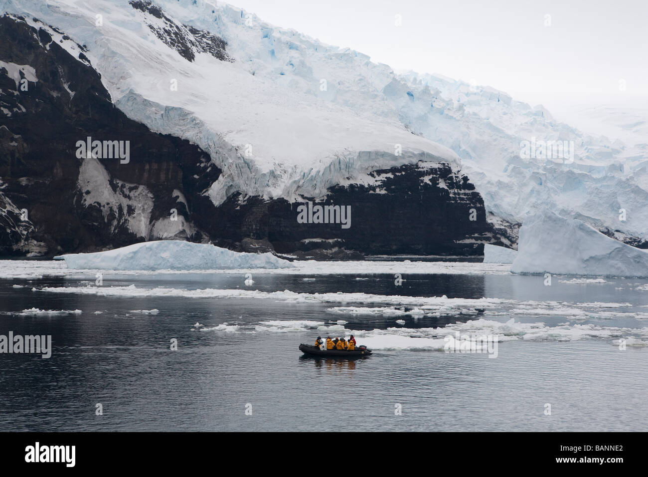 Turisti usano zodiac per esplorare San Pietro ho una remota isola e nei dintorni di ghiaccio e ghiacciai in mare Bellingshausen Antartide Foto Stock