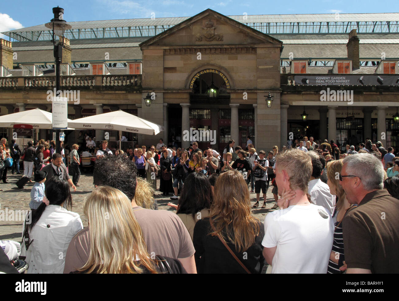 La folla di turisti a guardare gli artisti di strada musicista di strada sotto il sole al di fuori del mercato di Covent Garden di Londra. Foto Stock