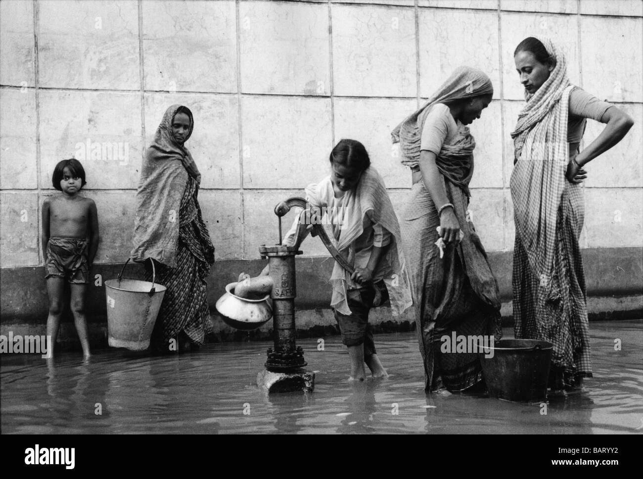Bangladesh Dhaka, le donne a un rifugio attingere acqua potabile da un tubo e che sta ancora lavorando a dispetto delle inondazioni. Foto Stock