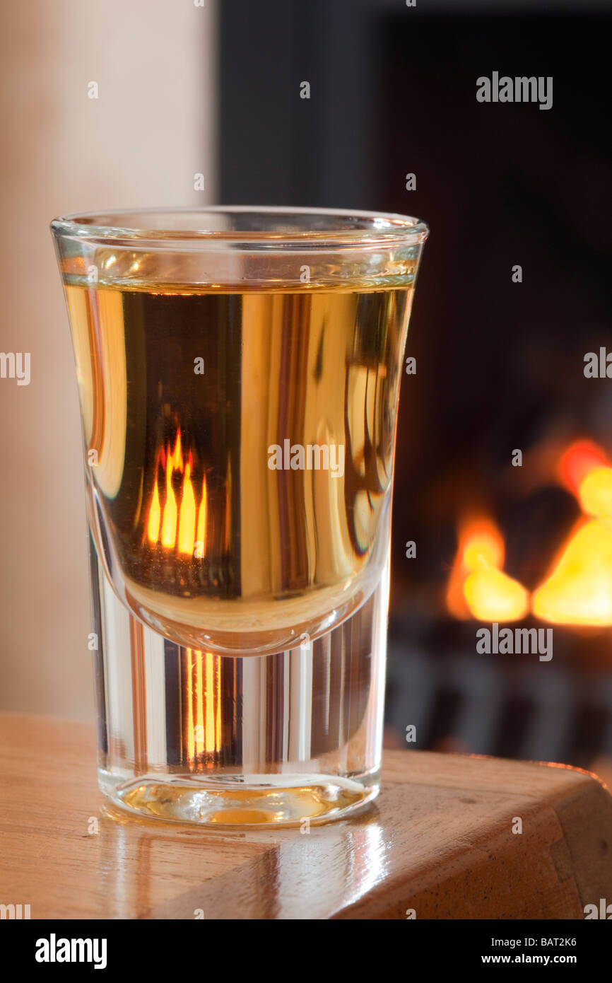 Di dram di riscaldamento di Scotch whisky di malto in un bicchiere di whiskey su di una tavola da aprire un fuoco di carbone England Regno Unito Gran Bretagna Foto Stock