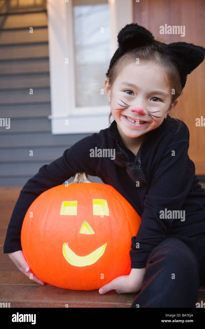 Razza mista giovane ragazza in costume gatto azienda zucca di Halloween Foto Stock