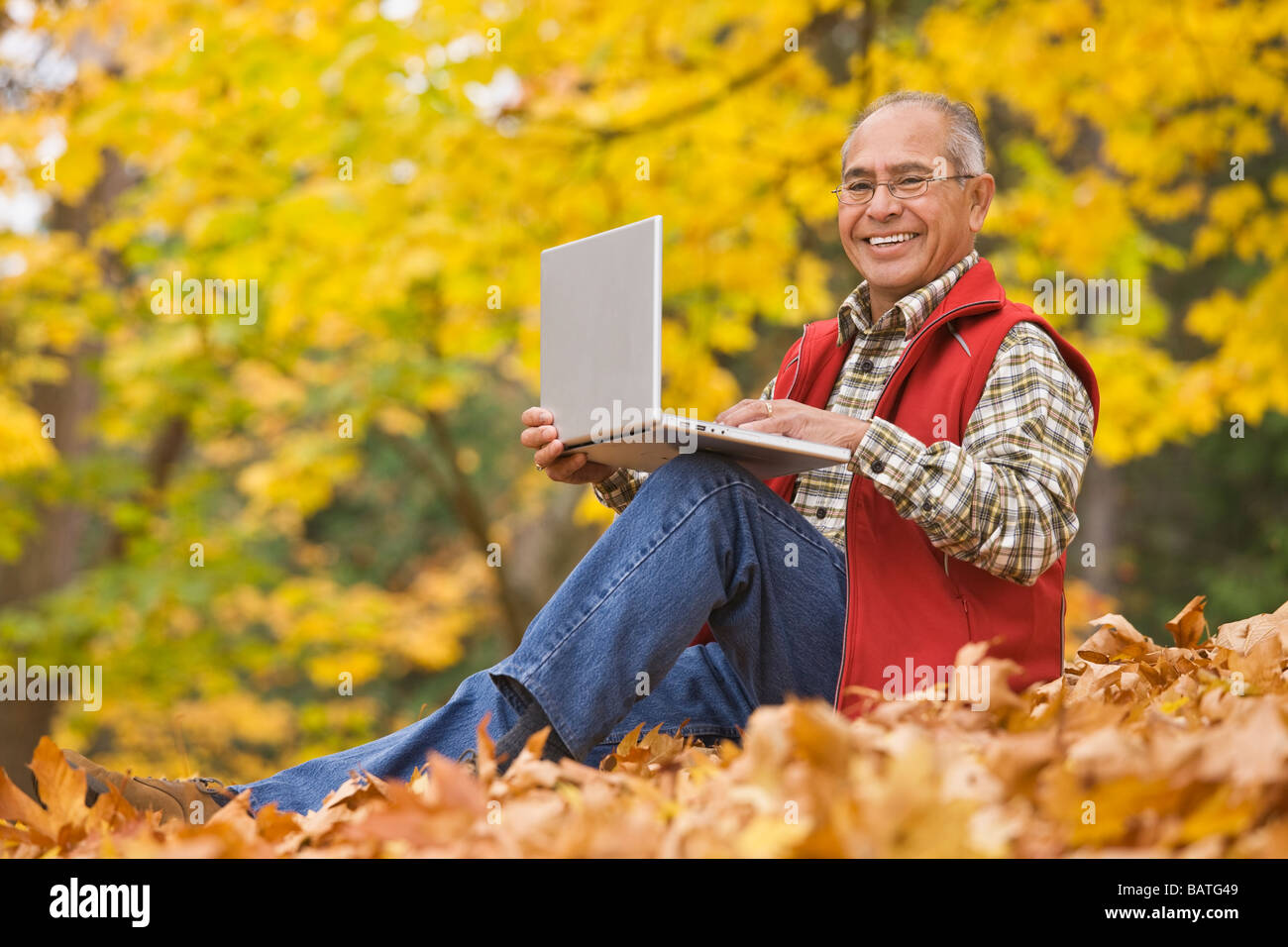 Uomo ispanico utilizzando laptop seduto in foglie di autunno Foto Stock