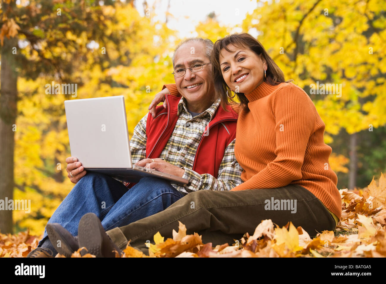 Coppia ispanica utilizzando laptop seduto in foglie di autunno Foto Stock