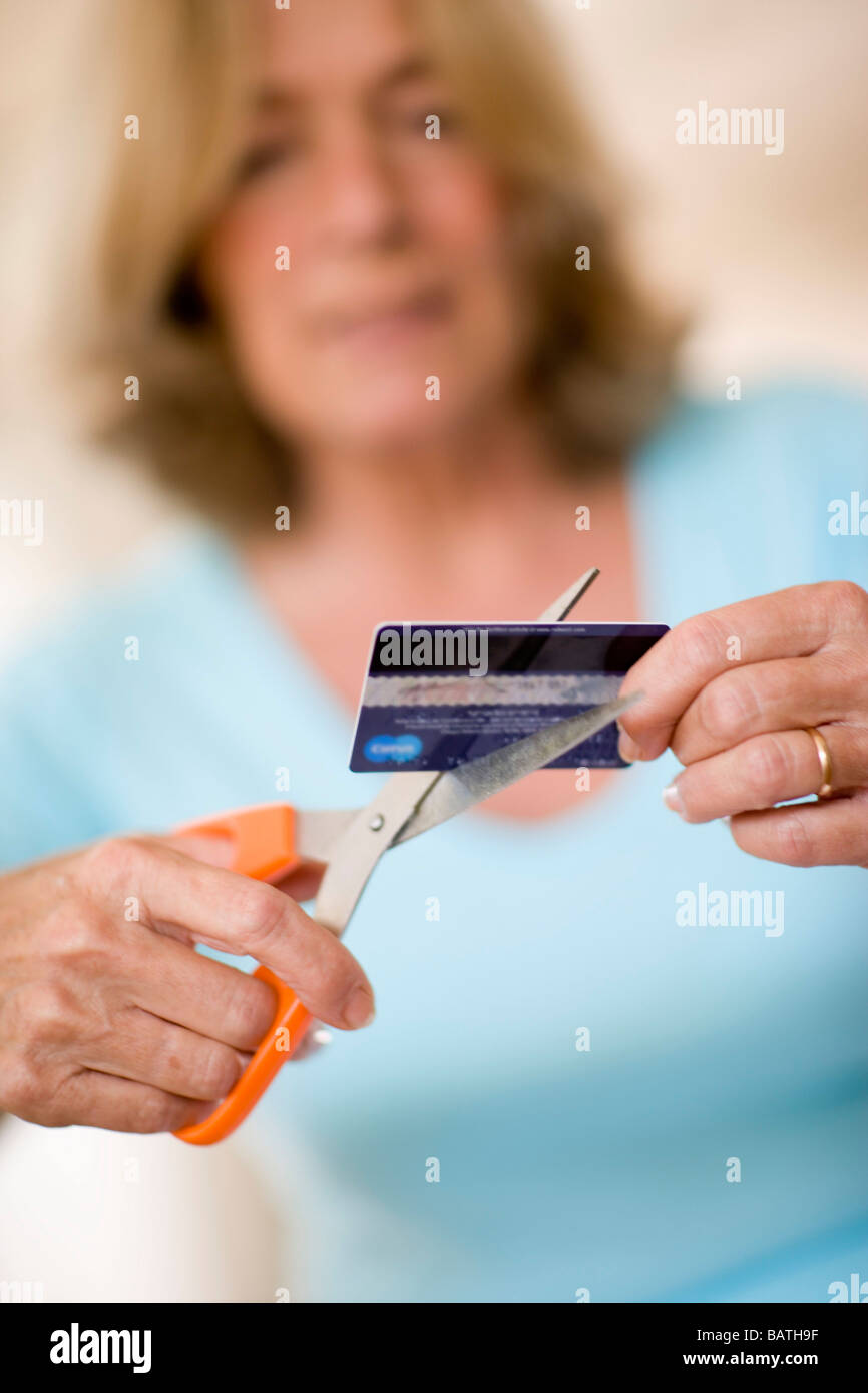Debito della carta di credito. Donna che utilizza un paio di forbici per tagliare la sua carta di credito. Foto Stock