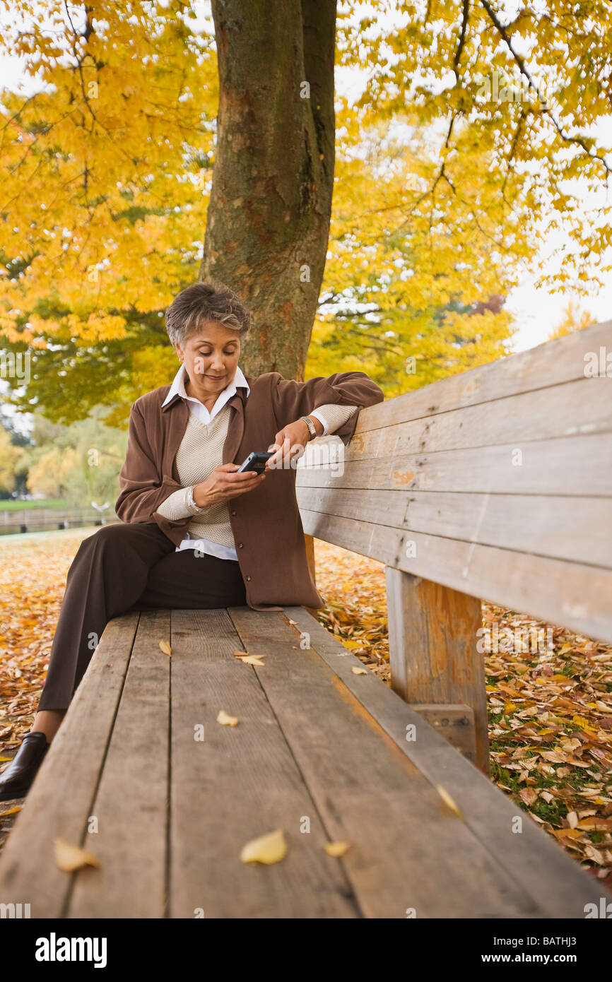 Donna africana tramite telefono cellulare su una panchina nel parco in autunno Foto Stock